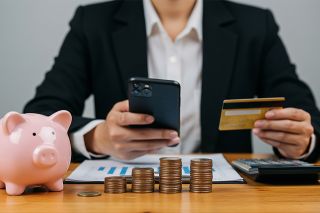 © Sultan - stock.adobe.com Foto: Mann mit Smartphone, Bankomatkarte, Sparschwein und Münzen